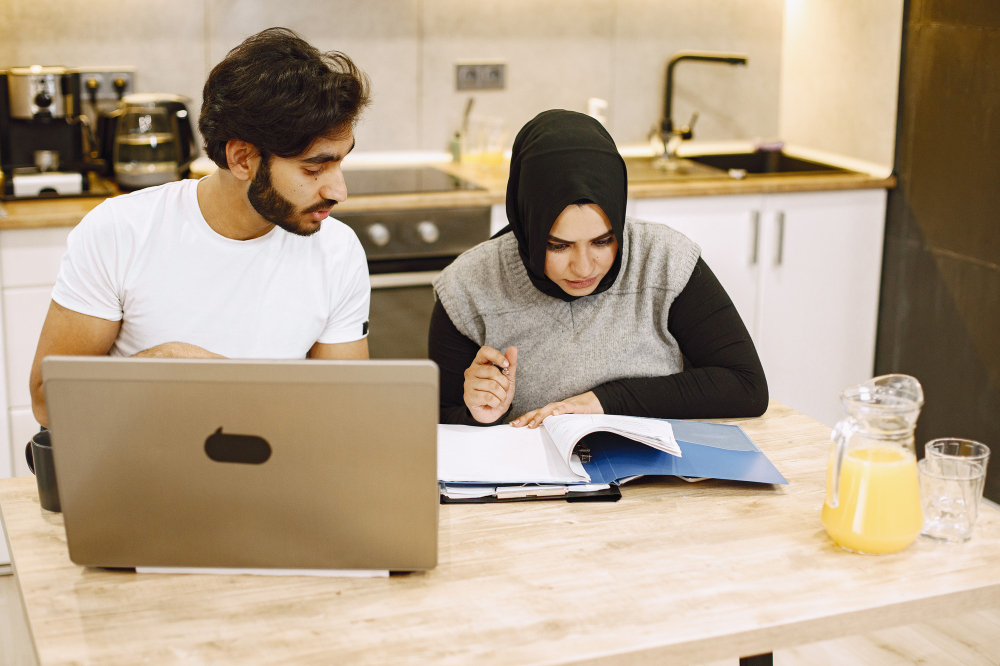 beautiful-young-couple-using-laptop-writing-notebook-sitting-kitchen-home-arab-girl-wearing-black-hidjab-1