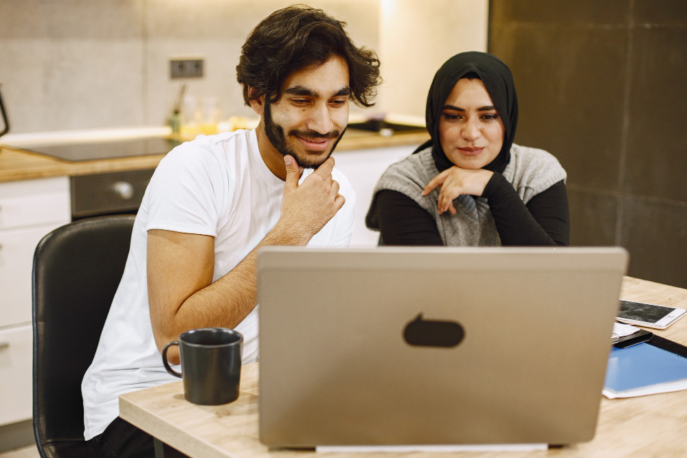 beautiful-young-couple-using-laptop-writing-notebook-sitting-kitchen-home-arab-girl-wearing-black-hidjab